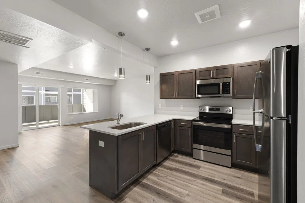 A modern kitchen with stainless steel appliances, dark wood cabinets, an island sink, and hardwood floors in a spacious open-plan area.