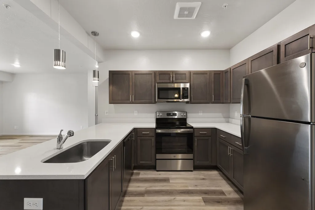 Modern kitchen with dark wood cabinets, stainless steel appliances, a double sink, and bright overhead lighting.
